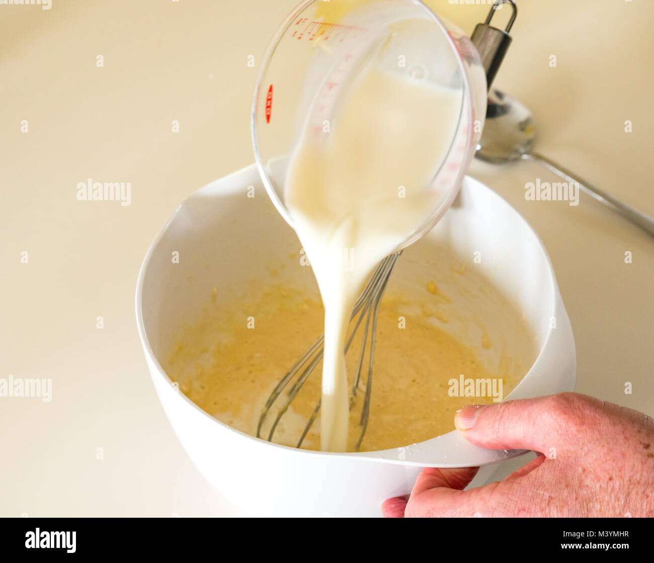 Man pouring milk à la pâte pour faire une pâte à crêpes pour Mardi Gras avec la farine, le lait, les œufs et l'huile dans une cuisine maison Banque D'Images