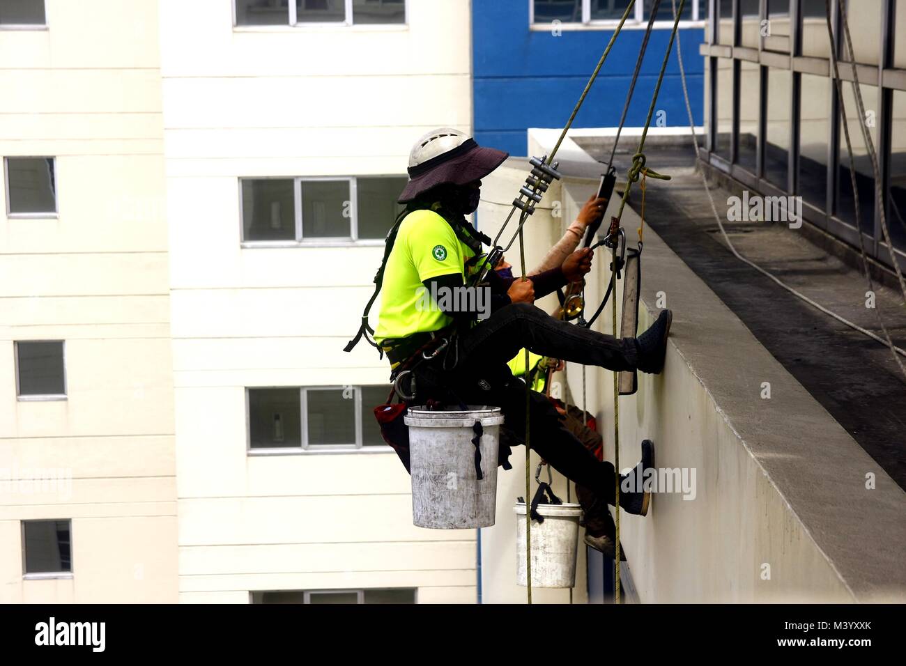 PASIG CITY, PHILIPPINES - le 7 février 2018 : nettoyage de vitres professionnel descendre l'extérieur d'un bâtiment à l'aide de cordes. Banque D'Images