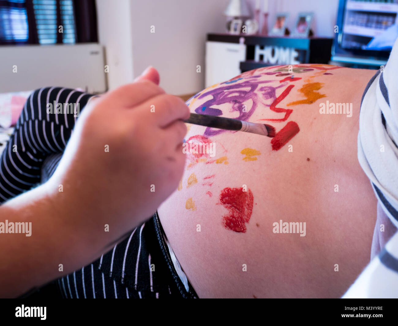 Petite fille mères peinture pregnant belly avec brosse à la maison close up Banque D'Images