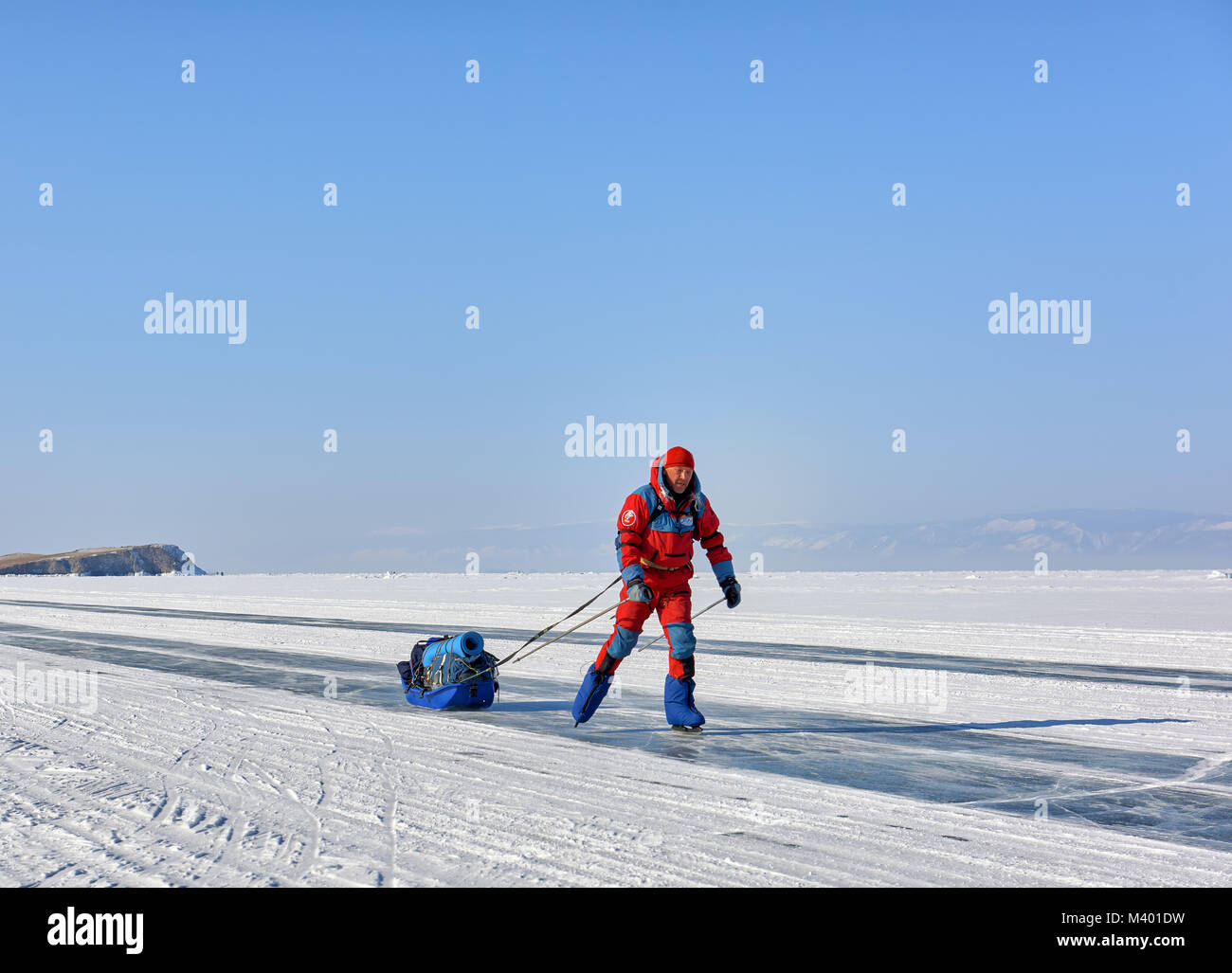 Le lac Baïkal, région d'Irkoutsk, RUSSIE - 08 mars 2017 : l'homme à une orange salopette polaire est le patinage. Vacances actives en hiver en Sibérie Banque D'Images