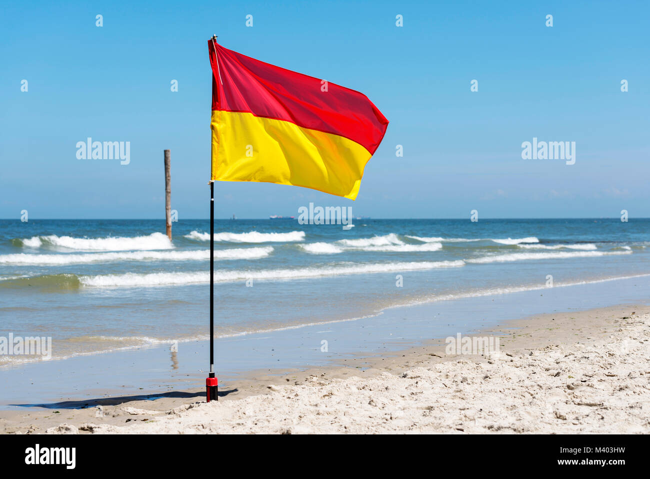 Panneau d'avertissement jaune et rouge d'un drapeau marquant la limite de la zone de baignade en toute sécurité sur une plage sous un ciel d'été bleu Banque D'Images