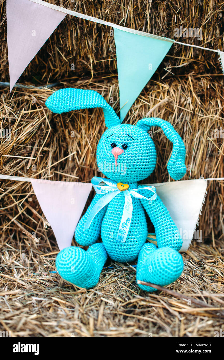 En peluche, lapin bleu sur la paille. Chaîne à la main des drapeaux bleu et rose sur l'arrière-plan. Style rustique Banque D'Images