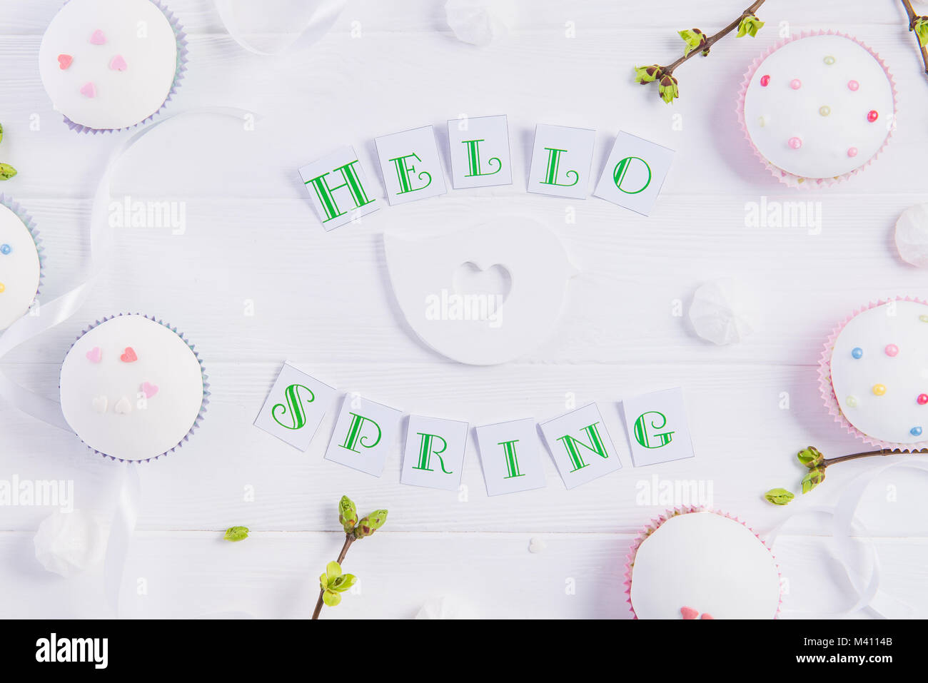 Vue supérieure de la composition de Bonjour printemps lettrage, branches avec de jeunes pousses de verdure, cupcakes de pâques bonbons, merengue, l'artisanat bird figure sur woo Banque D'Images