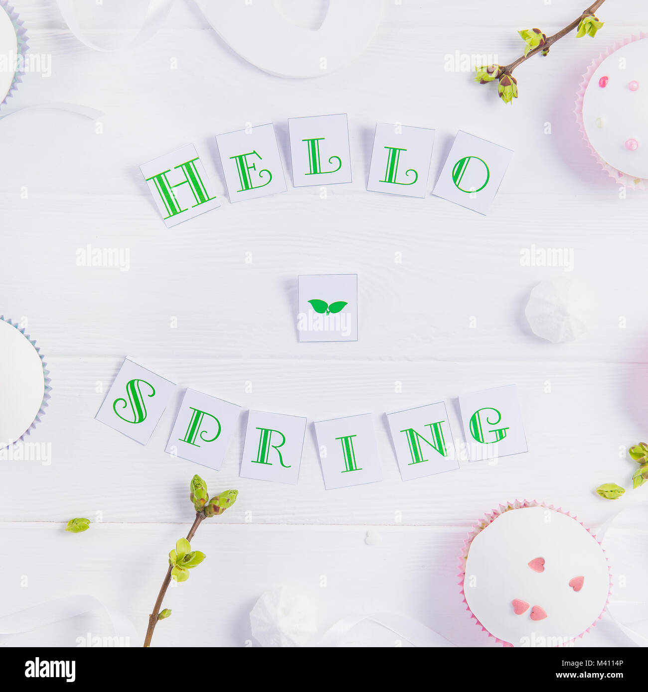 Vue supérieure de la composition de Bonjour printemps lettrage, branches avec de jeunes pousses de verdure, cupcakes de pâques bonbons, merengue, l'artisanat bird figure sur woo Banque D'Images