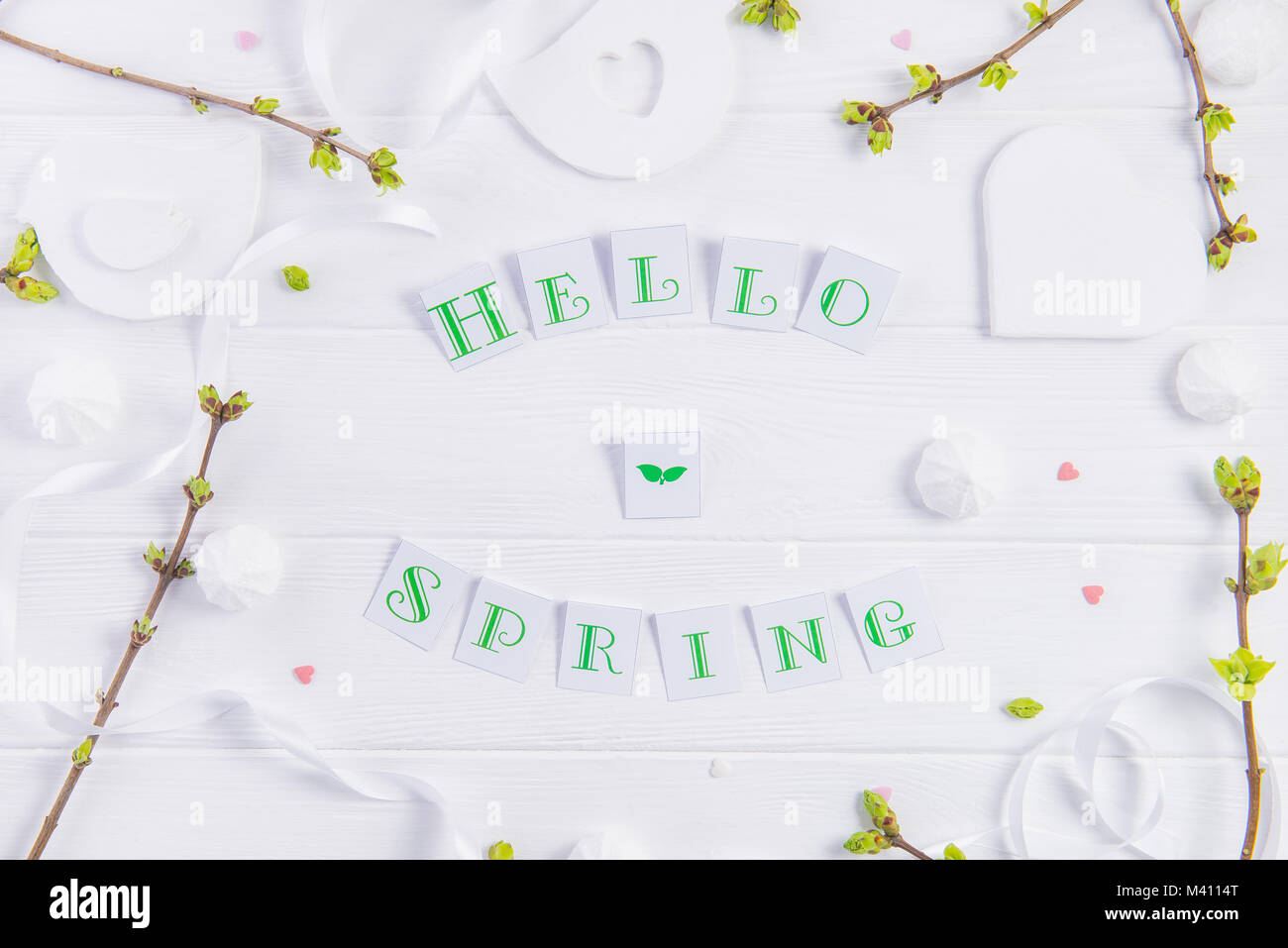 Vue supérieure de la composition de Bonjour printemps lettrage, branches avec de jeunes pousses de verdure, merengue et sucreries, bonbons coeur tricot bird figure sur woo Banque D'Images