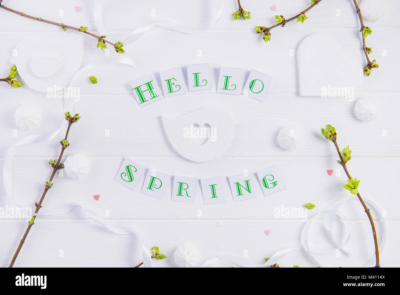 Vue supérieure de la composition de Bonjour printemps lettrage, branches avec de jeunes pousses de verdure, merengue et sucreries, bonbons coeur tricot bird figure sur woo Banque D'Images