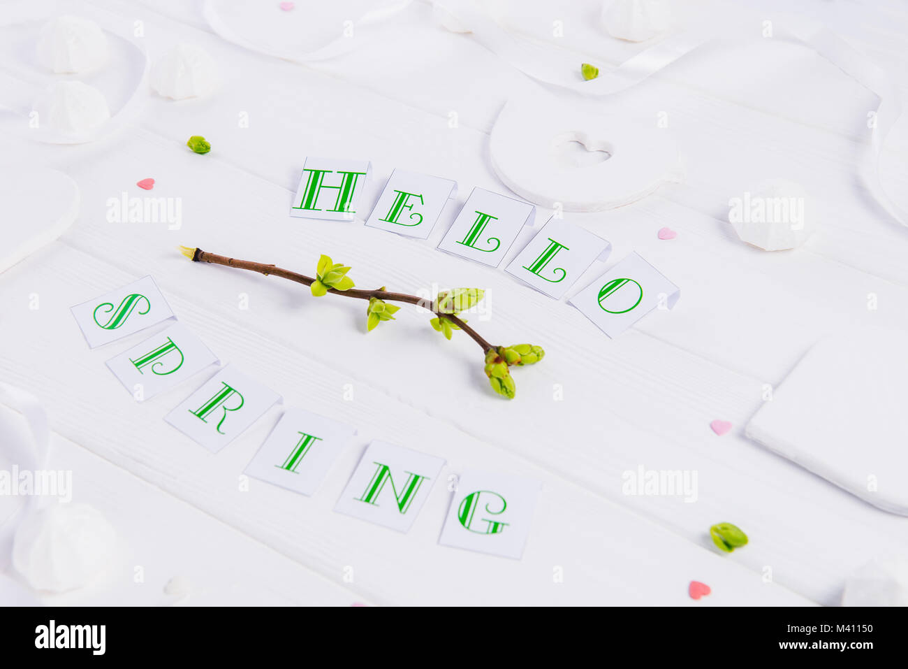 Close up composition de Bonjour printemps lettrage, branches avec de jeunes pousses de verdure, merengue et sucreries, bonbons coeur tricot bird figure sur woo Banque D'Images