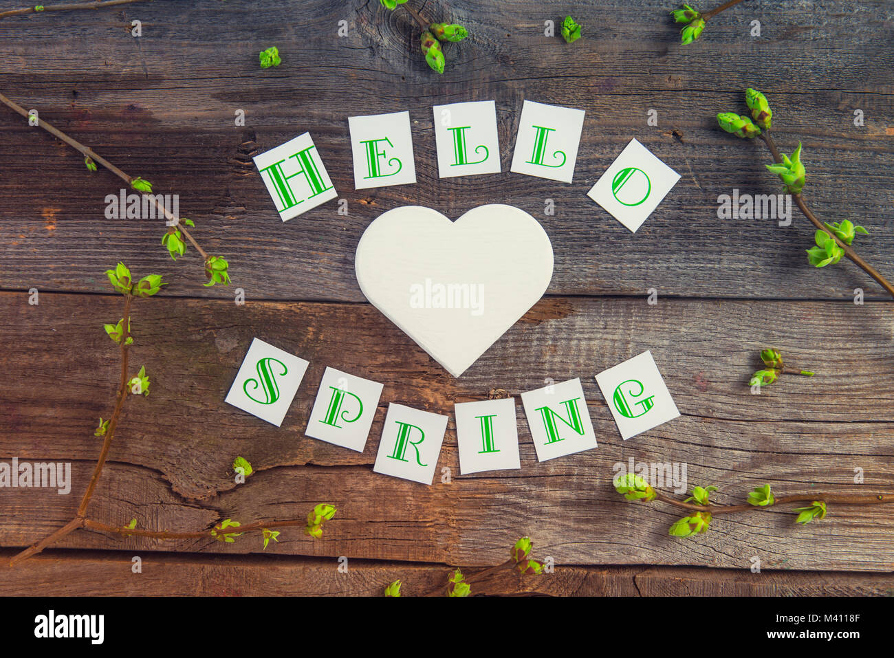 Vue supérieure de la composition de Bonjour printemps lettrage, branches avec de jeunes pousses de verdure et de l'artisanat bois blanc coeur figure sur bois rustique backgrou Banque D'Images