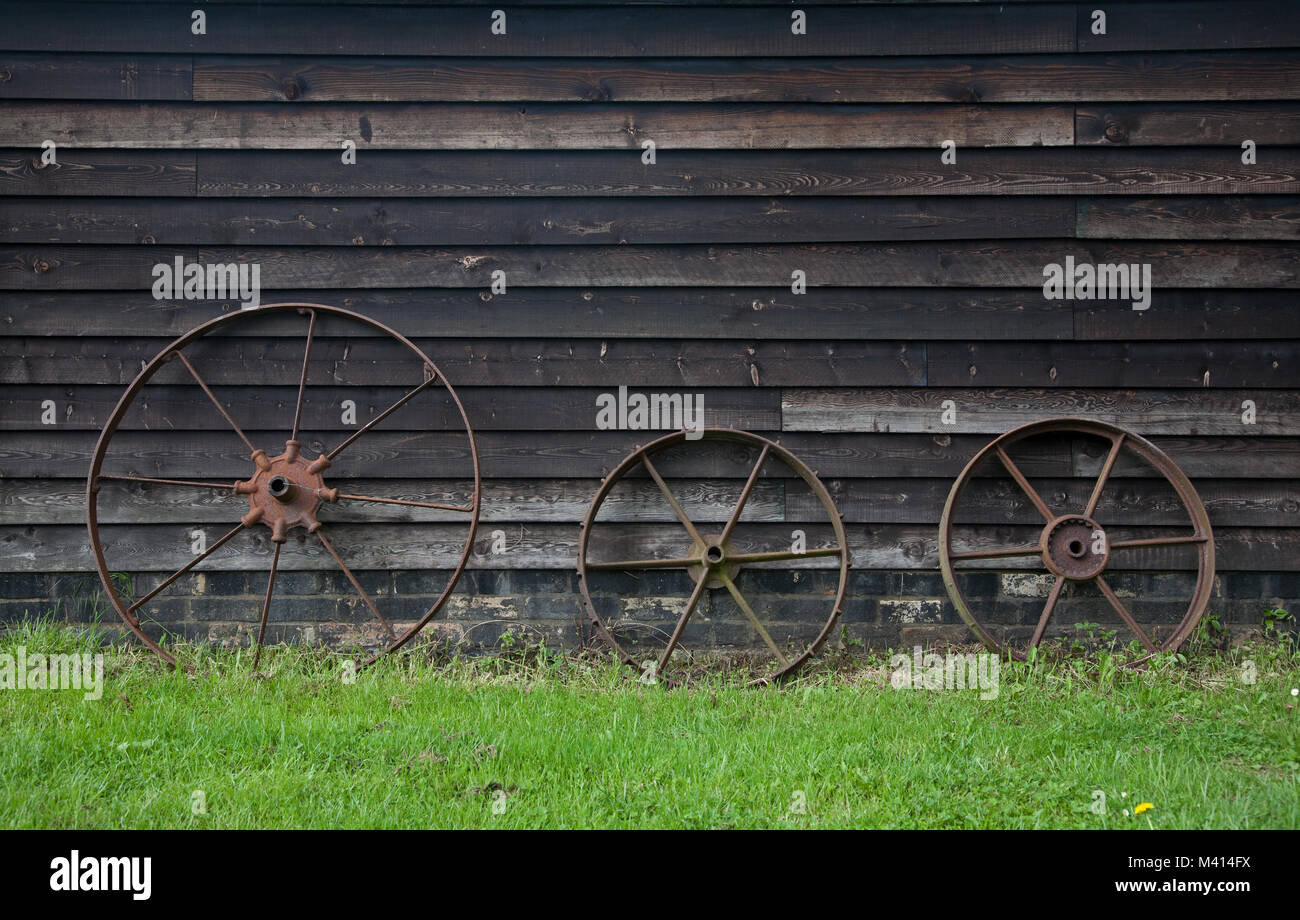 3 roues de chariot de rouille s'appuyer contre une grange en bois. Banque D'Images