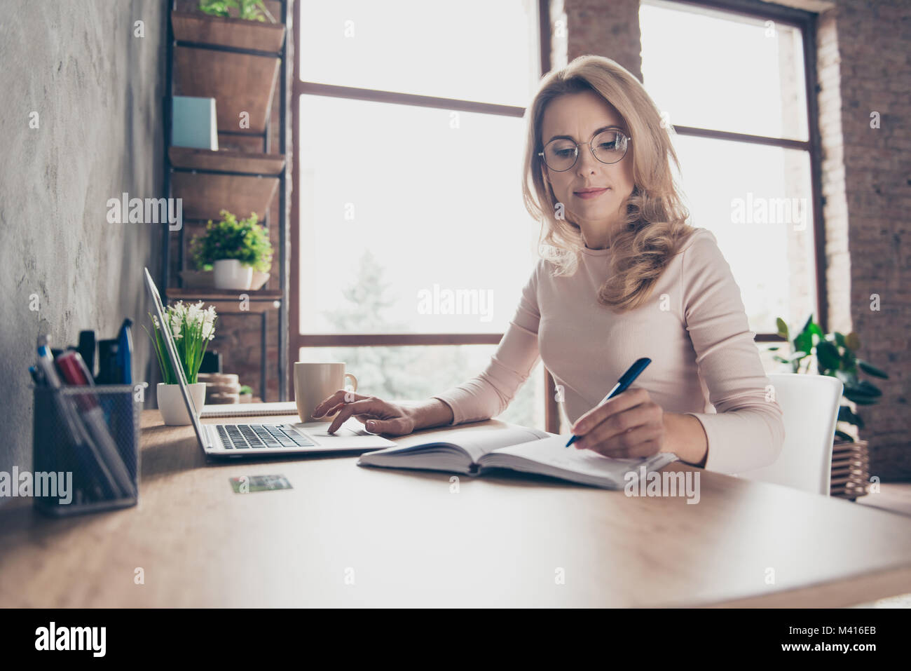 Portrait de beaux cheveux bouclés blonds avec confiance clever femme portant des vêtements décontractés, elle est assise à la table en face de l'ordinateur et vérifier Banque D'Images