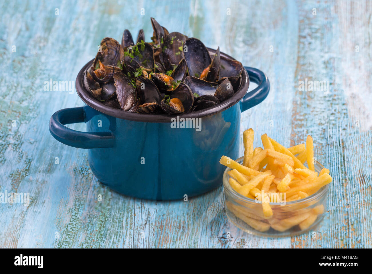Moules dans un pot en céramique bleu sur un fond de bois bleu. avec un bol en verre de frites. Brlgium de vie. Banque D'Images