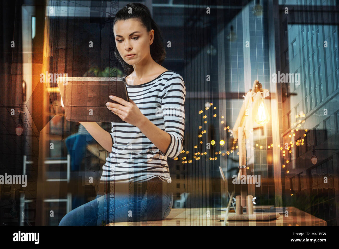 Femme sérieuse à la recherche de son appareil et assis sur la table Banque D'Images