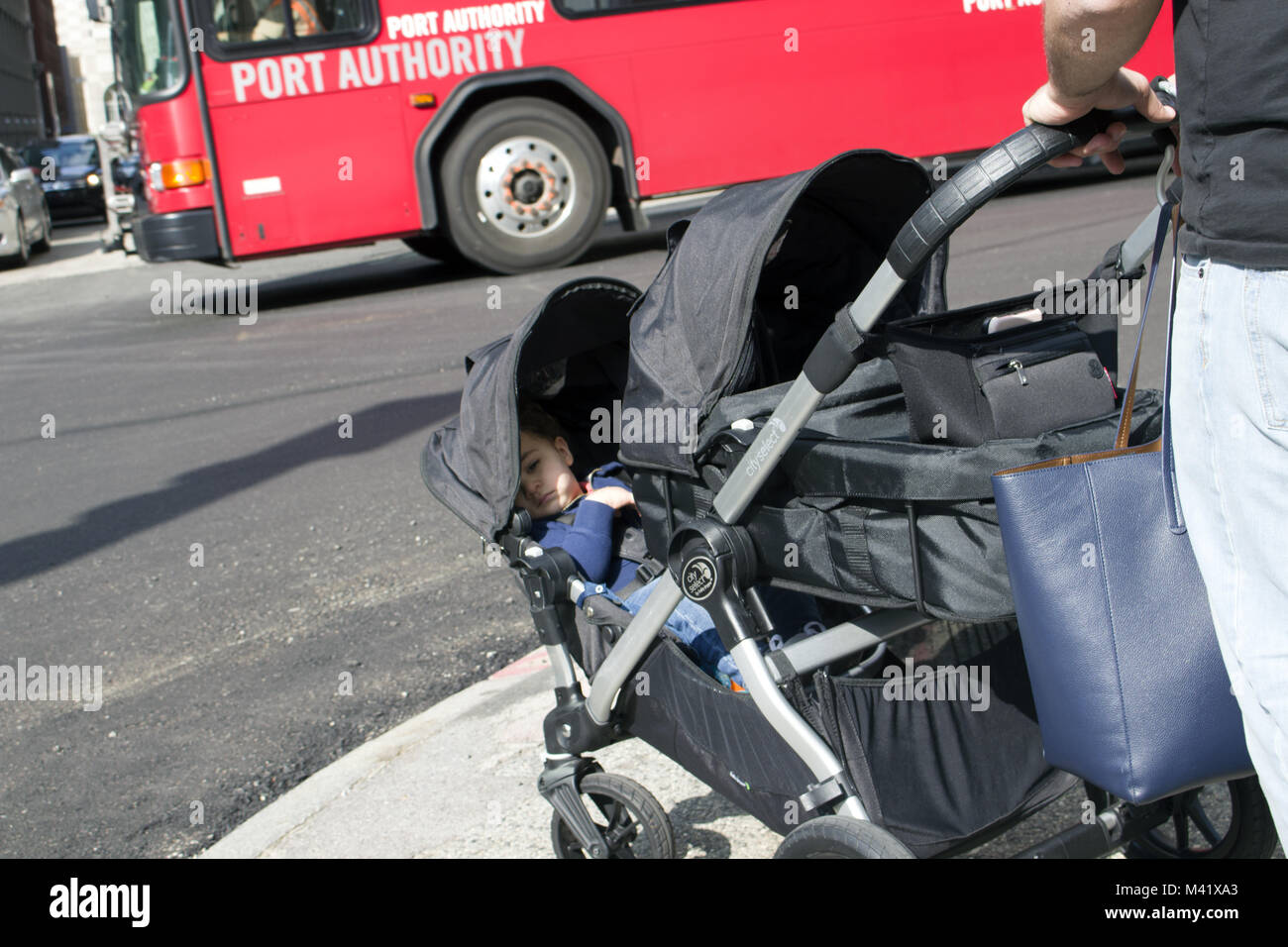 Enfant dans une poussette sur un trottoir qui est poussé par leurs parents. Banque D'Images