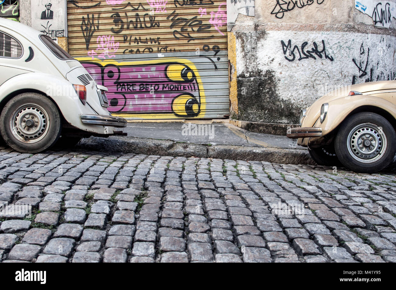 Deux vieux Volkswagen voitures garées sur une rue pavée en face d'un mur recouvert de graffitis à Rio de Janeiro, Brésil Banque D'Images