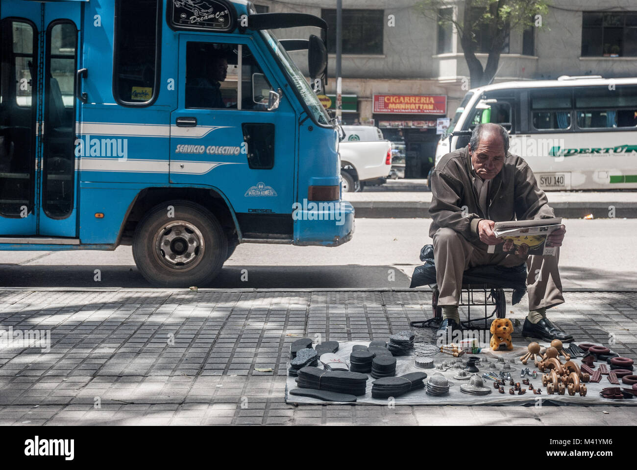 Un vieil homme lisant un journal et la vente d'articles de maison à côté d'un bus public bleu sur rue à Bogota, Colombie Banque D'Images