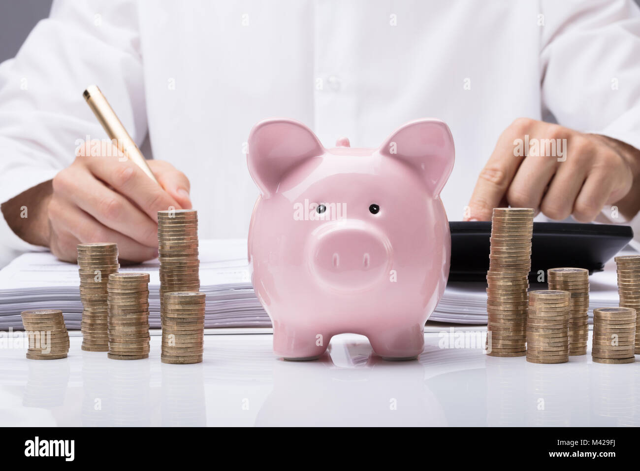 Close-up of Businessman Calcul Loi Avec Piggybank et empilés pièces sur Desk In Office Banque D'Images