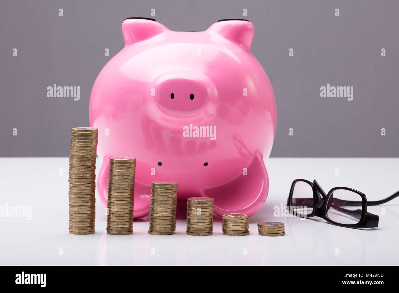 Tirelire à l'envers sur la table avec les lunettes et les pièces empilées sur la table Banque D'Images