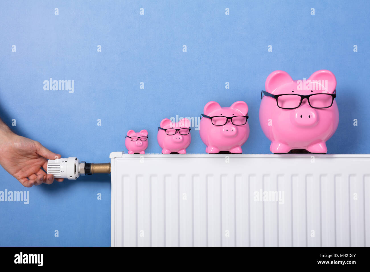 Close-up of a person's Hand avec thermostat de réglage Piggy Banks Wearing Eyeglasses sur radiateur Banque D'Images