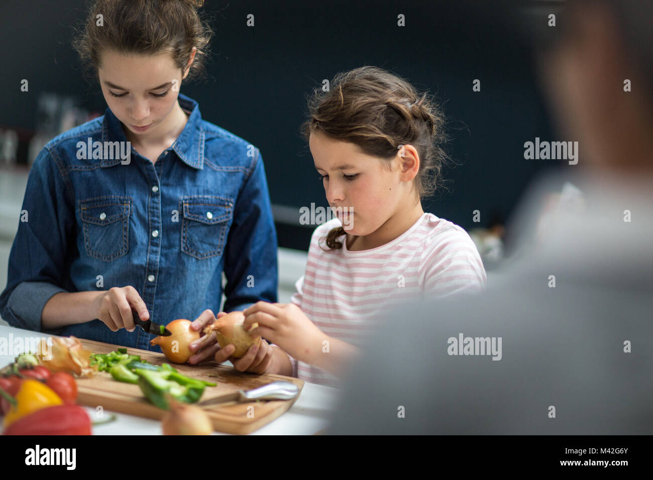 Maman regardant filles couper les légumes Banque D'Images