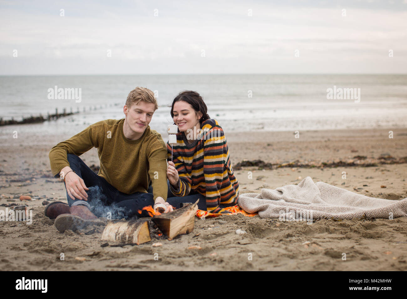 Jeune couple toasting guimauves sur feu de camp Banque D'Images