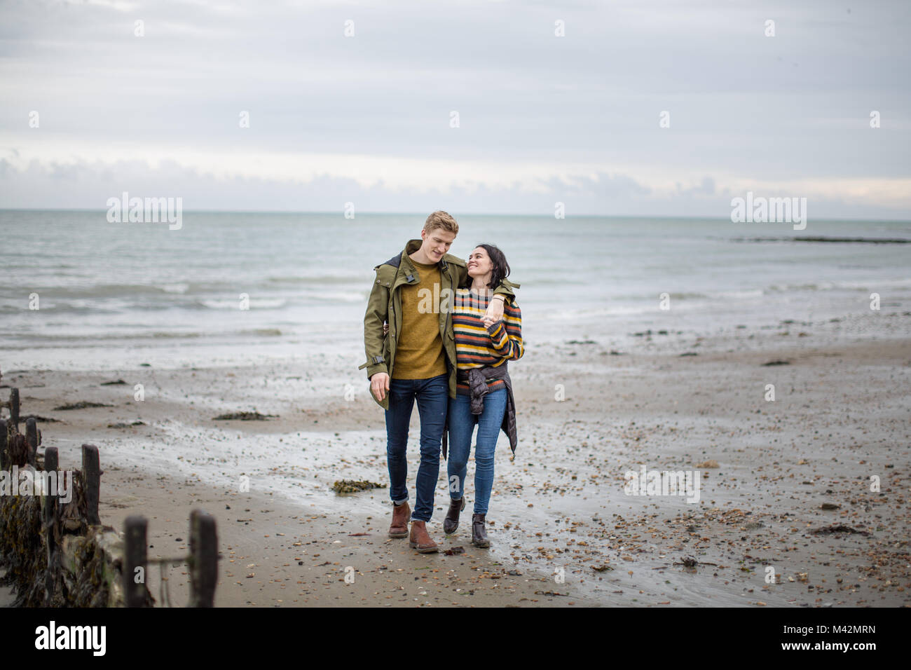 Jeune couple en train de marcher sur une plage en hiver Banque D'Images