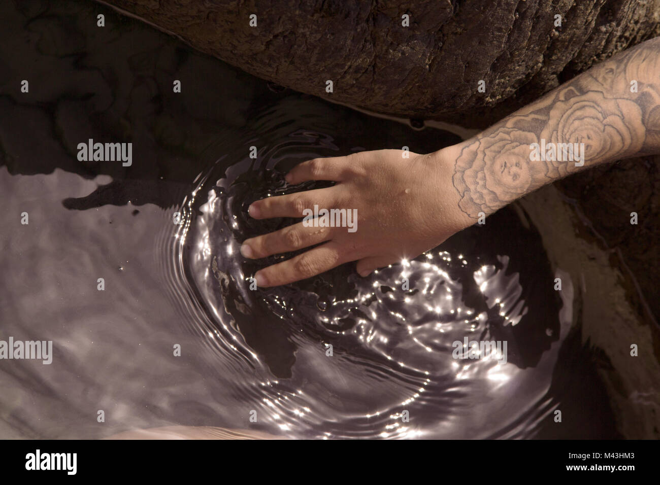 Close up of woman with tattoo plongeant sa main dans l'eau d'une piscine dans les rochers Banque D'Images