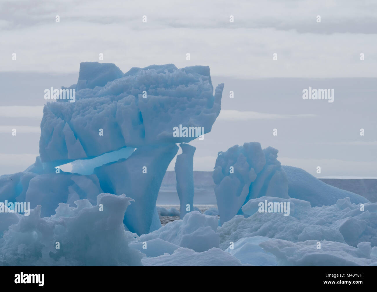 Un iceberg bleu flottant dans l'eau gris foncé de l'océan Austral au son de l'Antarctique. Ciel couvert et d'un continent de la neige sont à l'arrière-plan Banque D'Images