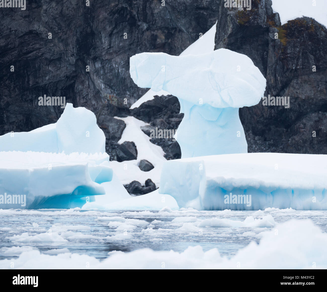 Une étrange formation de glace sur un iceberg bleu clair avec les rochers escarpés de l'Antarctique dans l'arrière-plan. Photographié dans Cierva Cove. Banque D'Images