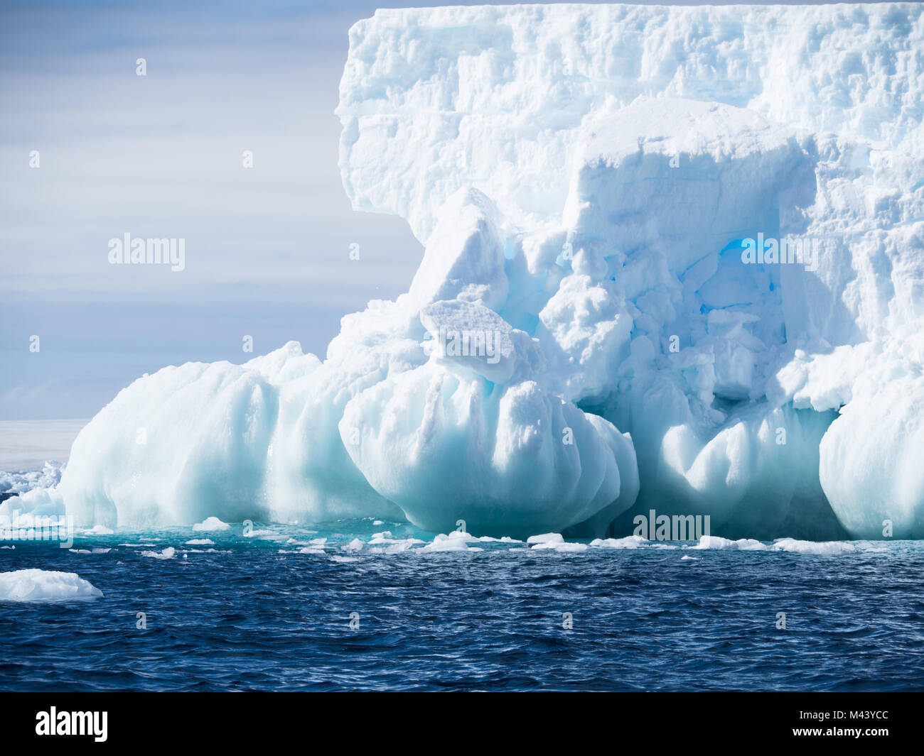 Un grand iceberg bleu clair avec une fondation de sphères. L'eau bleu foncé de l'océan Austral a petites rides. ciel nuageux au-dessus. Banque D'Images