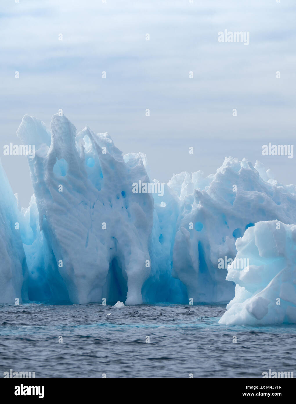 Un léger, moyen et bleu foncé iceberg flottant dans l'eau gris foncé de l'océan Austral au son de l'Antarctique. Ciel couvert et d'un continent de la neige sont Banque D'Images
