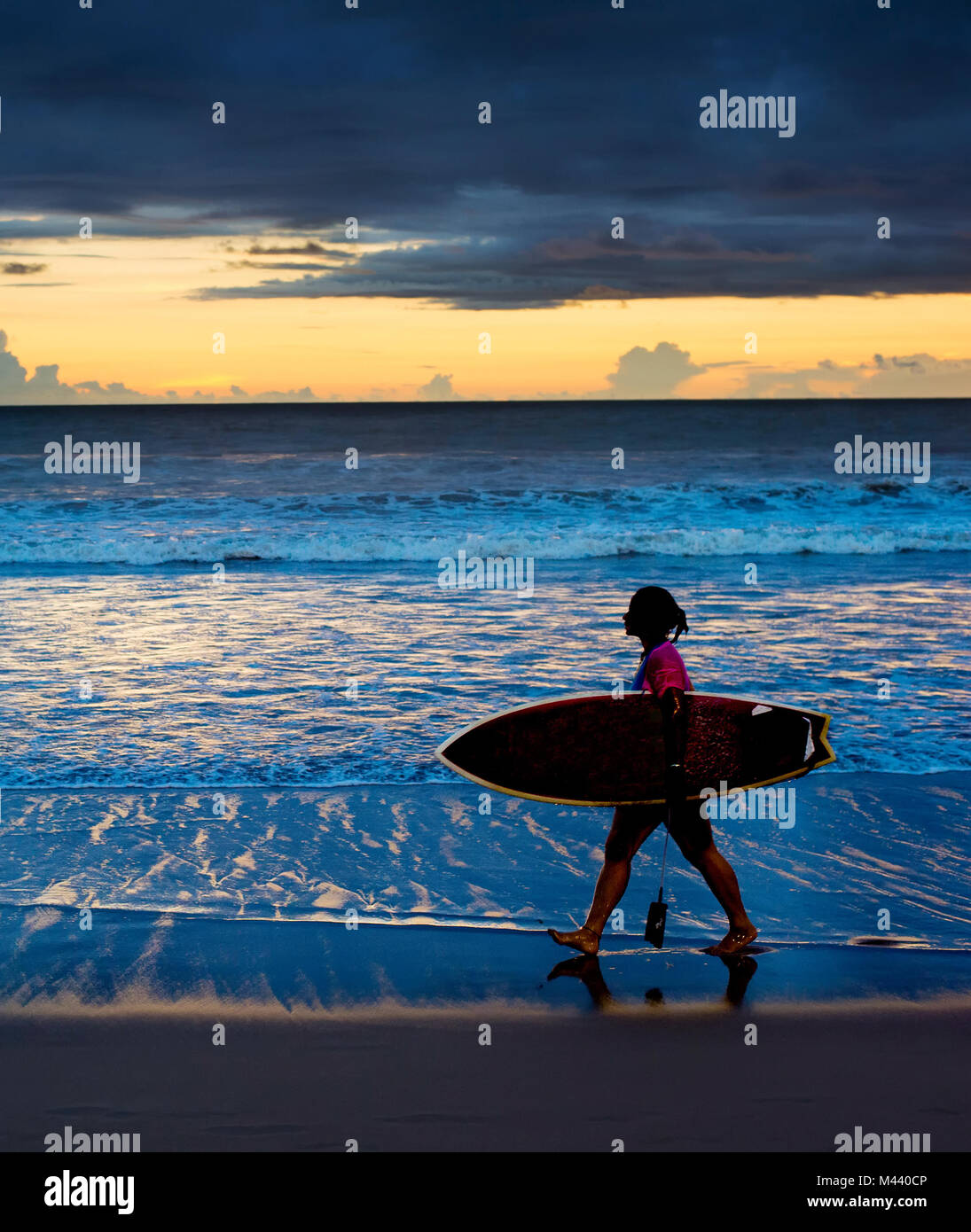 Surfgirl marche sur la plage avec une planche de surf au coucher du soleil. L'île de Bali Banque D'Images