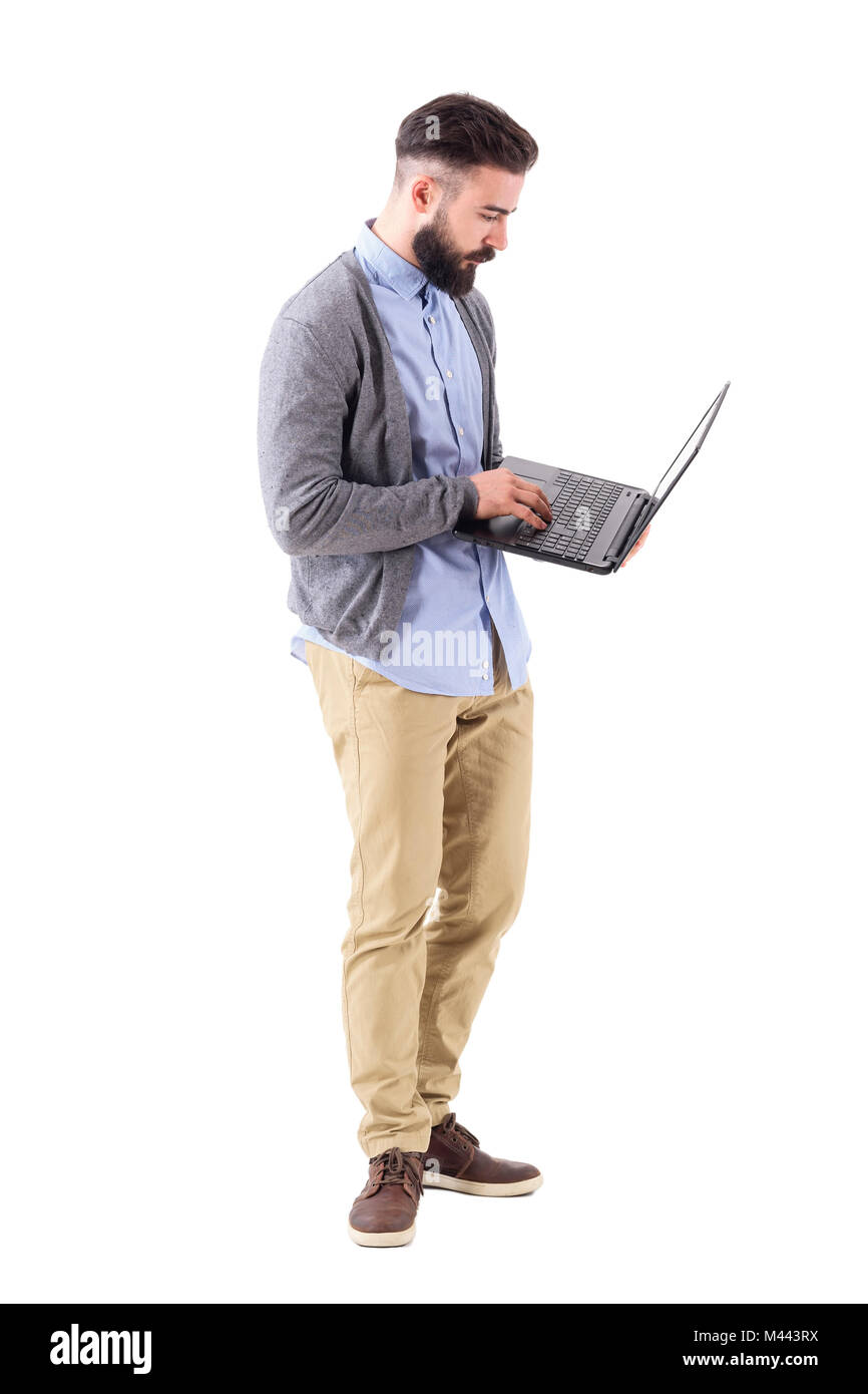 Vue latérale d'homme barbu élégant de la saisie sur clavier d'ordinateur portable à la recherche à l'ordinateur. La pleine longueur du corps portrait isolé sur fond blanc studio. Banque D'Images
