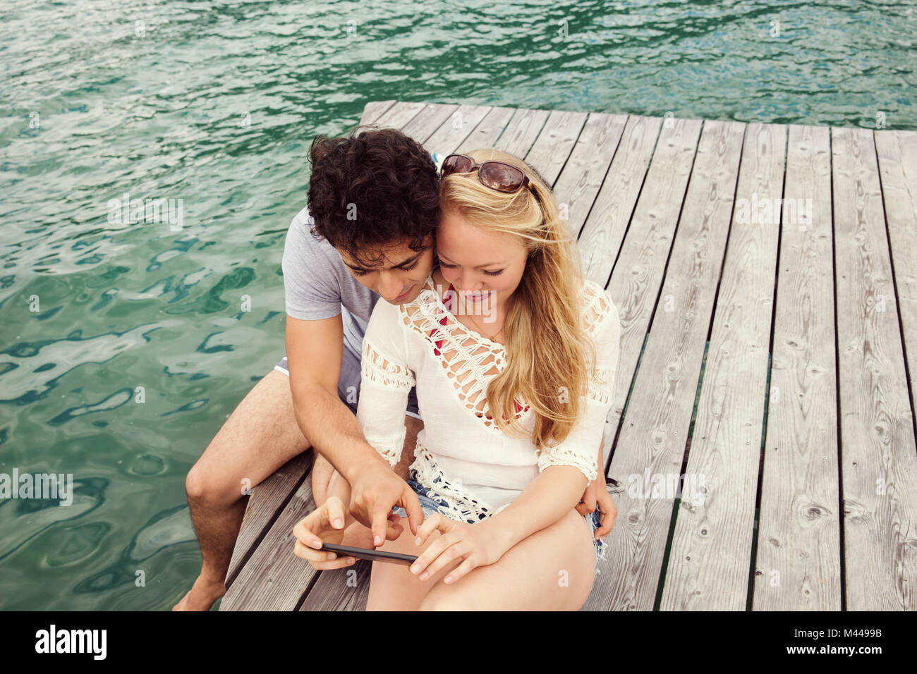 Couple sitting on pier looking at smartphone Banque D'Images