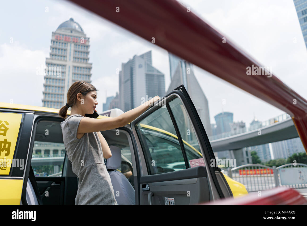 Young businesswoman getting out of yellow cab au centre financier de Shanghai, Shanghai, Chine Banque D'Images