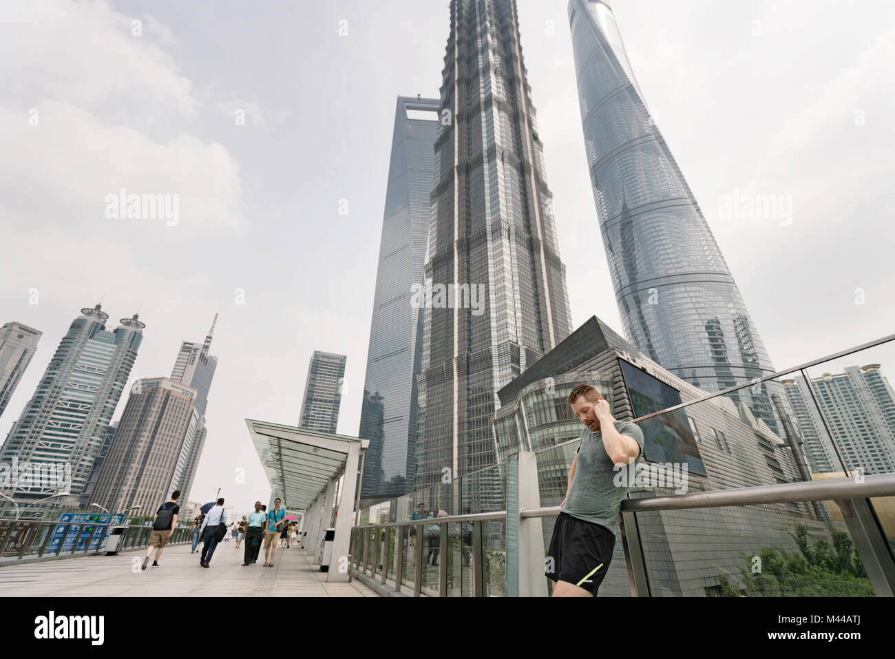 Young male runner appuyé contre la rampe d'écouteurs de réglage dans le centre financier de Shanghai, Shanghai, Chine Banque D'Images