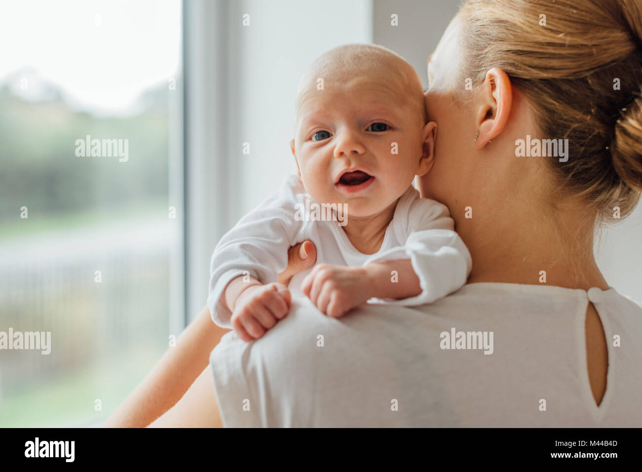 Young woman holding baby daughter, over Shoulder portrait Banque D'Images