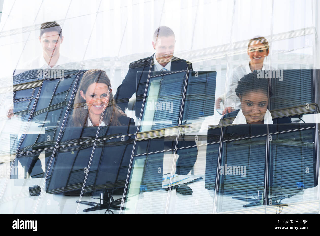 Les gens d'affaires multiethniques en utilisant des ordinateurs de bureau en verre bureau vu par Banque D'Images