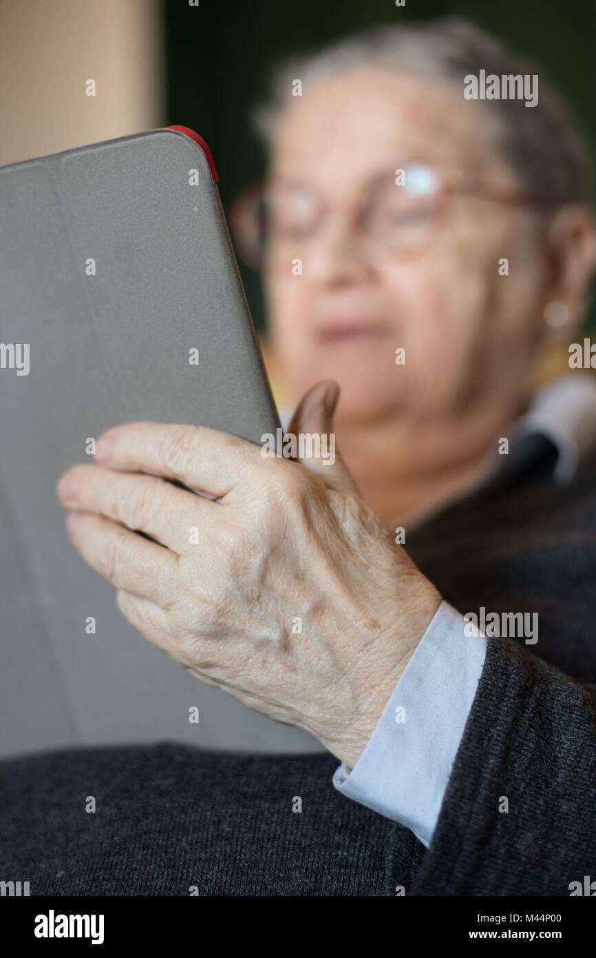 Femme âgée à la maison assis sur le canapé à l'aide de tablet e-book portrait focus sélectif sur les mains Banque D'Images