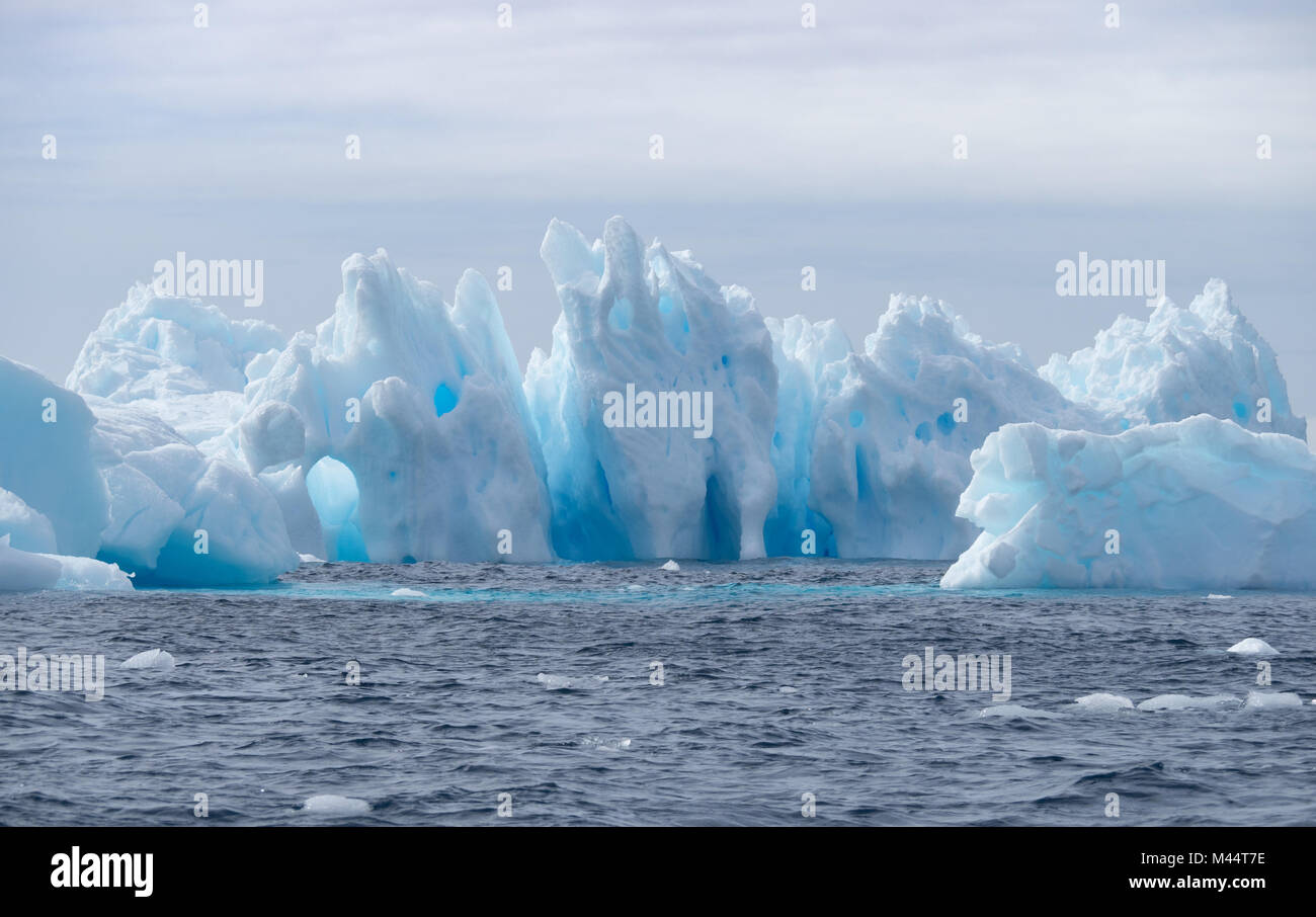 Une lumière bleu moyen et iceberg flottant dans l'eau gris foncé de l'océan Austral au son de l'Antarctique. Ciel couvert est ci-dessus. Banque D'Images