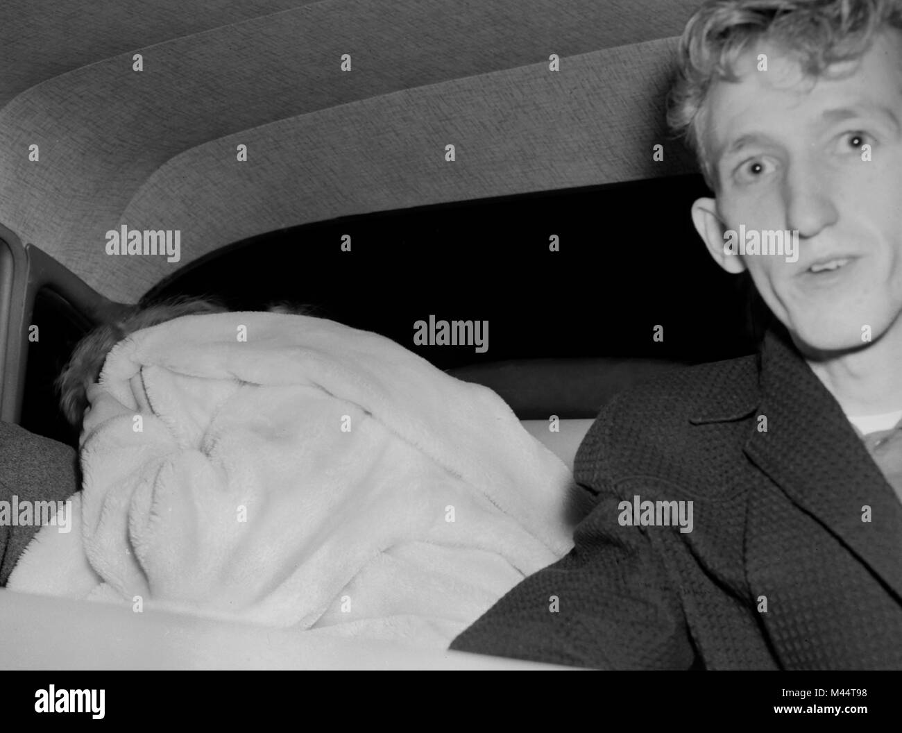 L'un des deux suspects de siège se cache de la caméra dans une voiture de police, ca. 1950. Banque D'Images