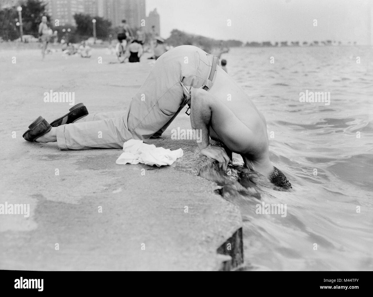 Un homme refroidit le long de Oak Street Beach à Chicago en collant sa tête dans le lac MIchigan, ca. 1955. Banque D'Images