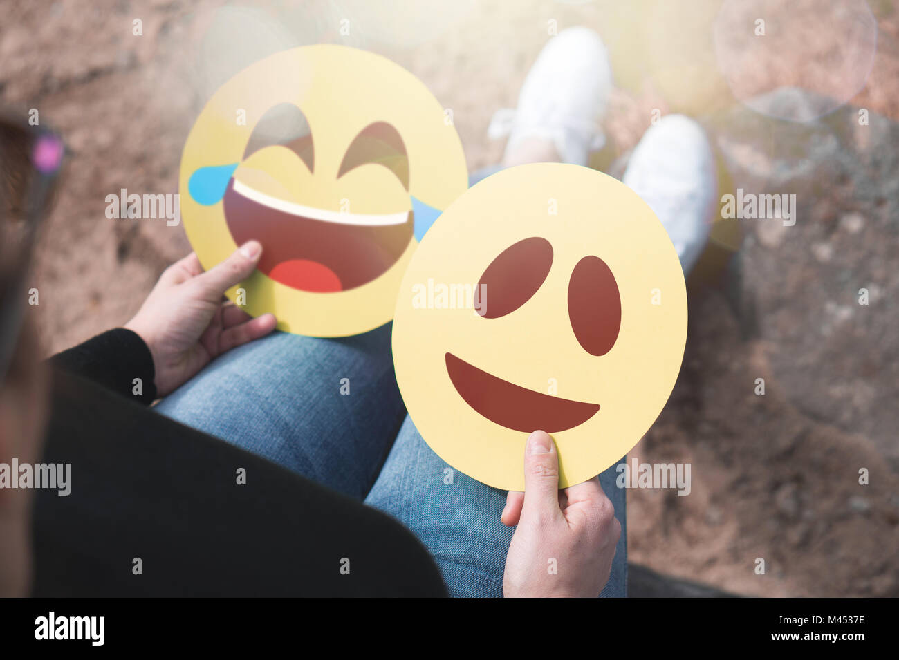 Woman holding 2 émoticônes en carton dans la main. Heureux de rire et sourire. Deux icônes modernes de communication et d'expression imprimée sur papier. Banque D'Images