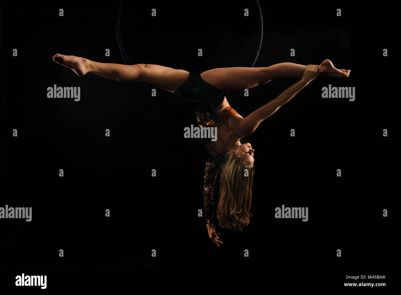 Jeune femme faisant acrobat aériennes groupes tête en bas de hoop, fond noir Banque D'Images