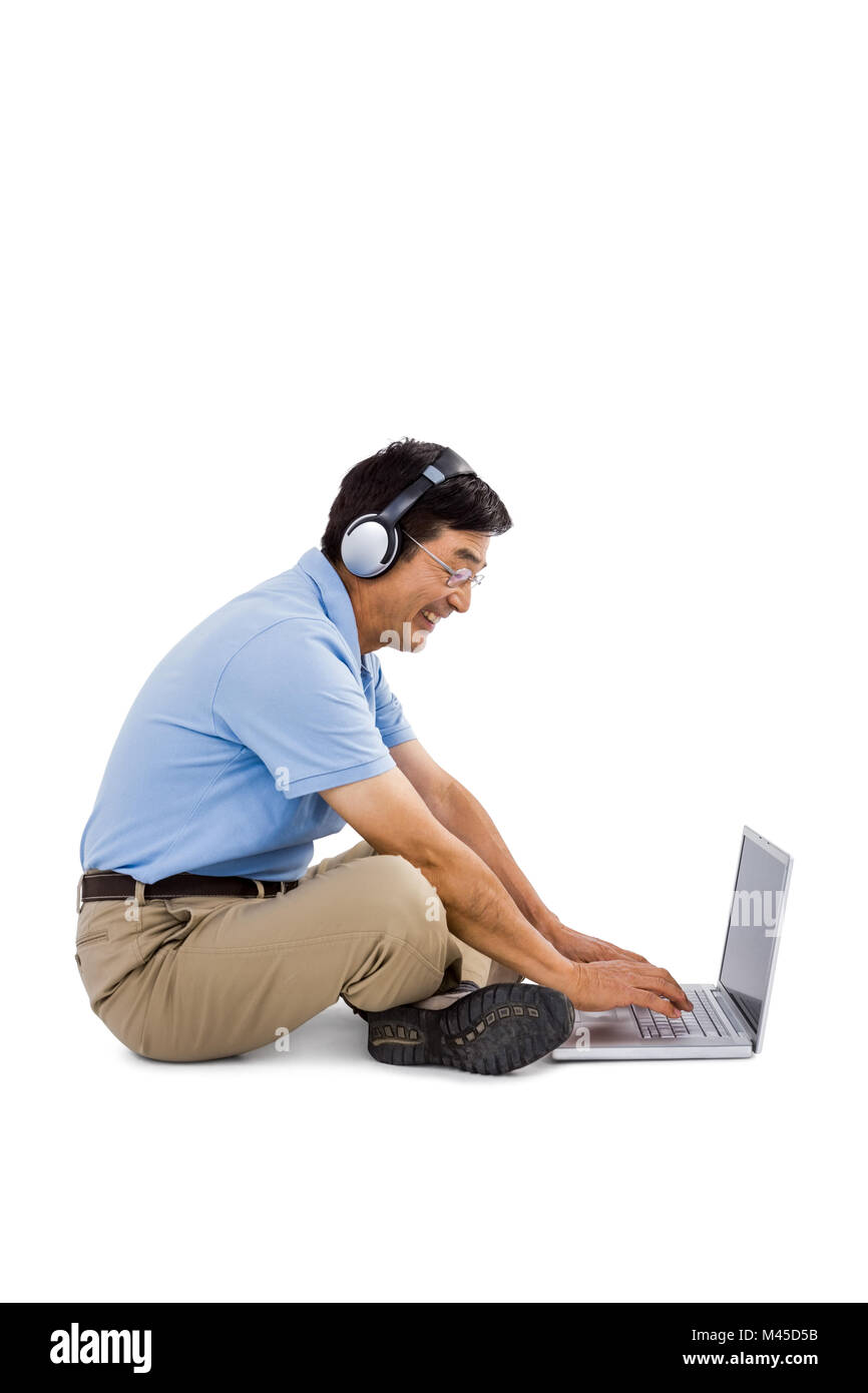 Vue latérale du cheerful man listening music while using laptop Banque D'Images