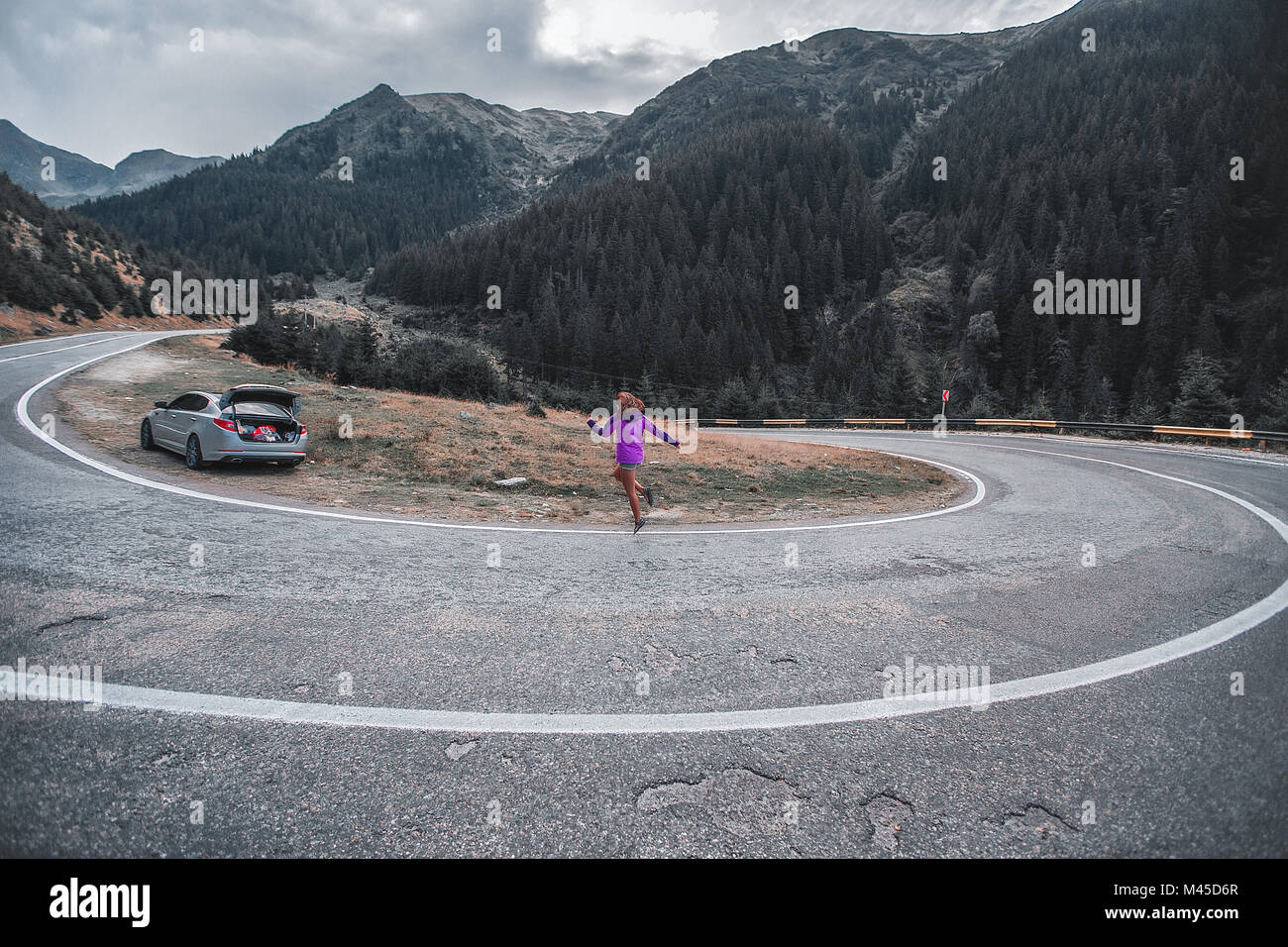 Jeune femme sautant sur route de montagne avec virage en épingle, Draja, Vaslui, Roumanie Banque D'Images