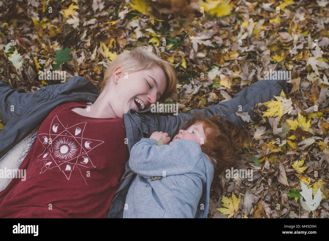 Femme aux cheveux rouge tout-petit et jeune femme couchée sur les feuilles d'automne Banque D'Images