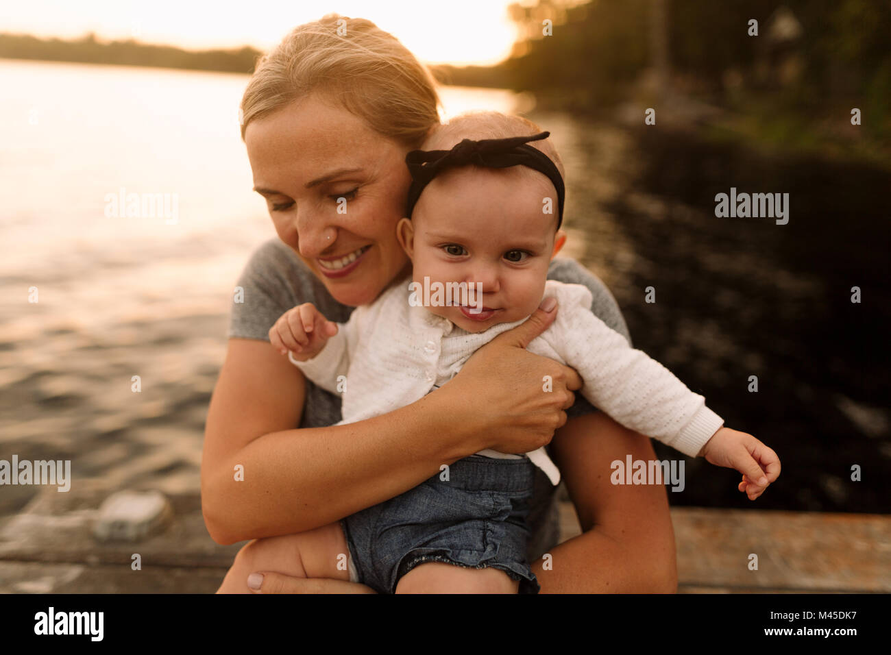 Mother sitting on pier hugging baby daughter Banque D'Images