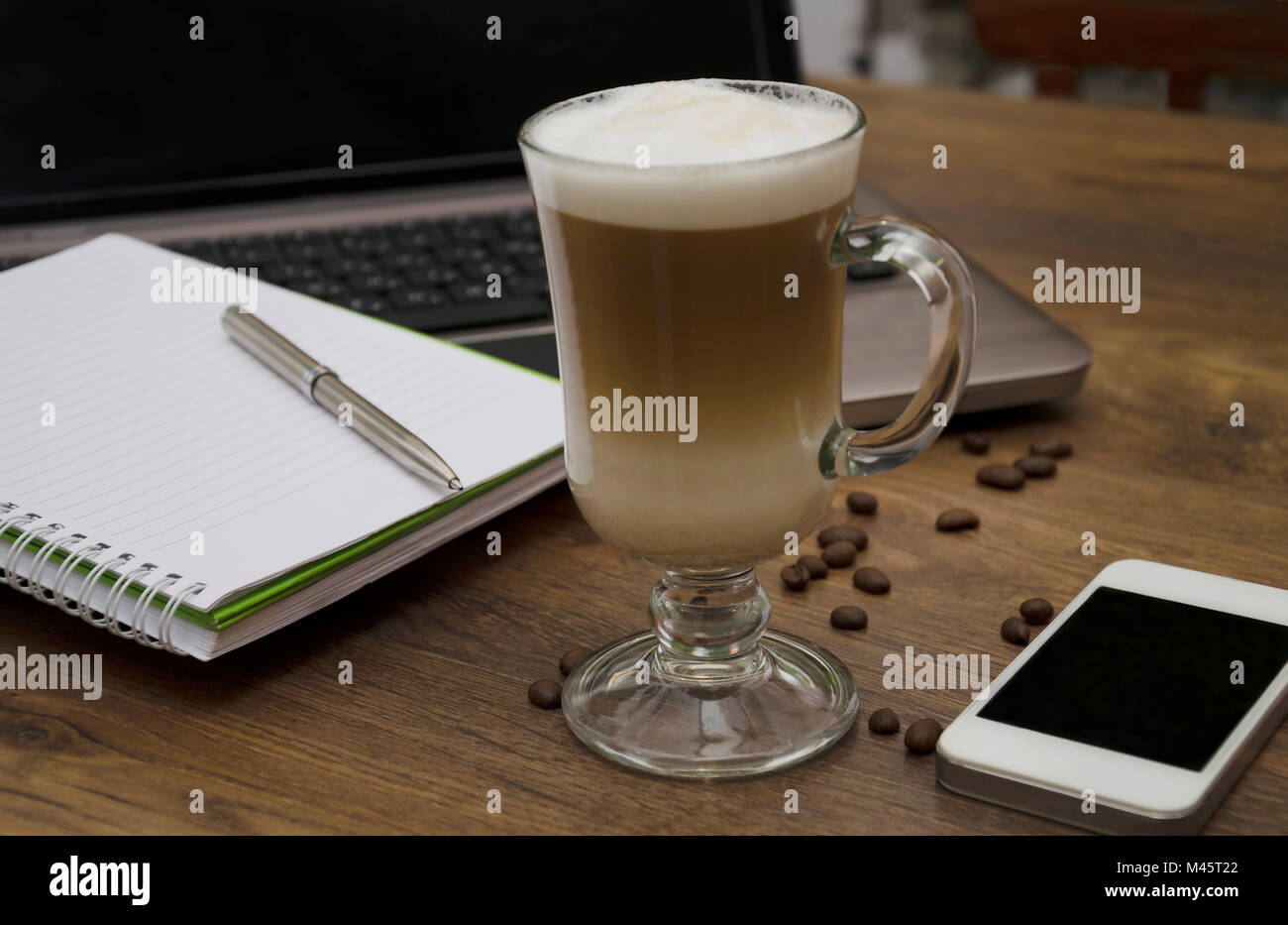 Boisson chaude avec du café et du lait, latte, cappuccino, dans un beau verre, verre, le bloc-notes de téléphone et un stylo sur le fond de l'ordinateur Banque D'Images