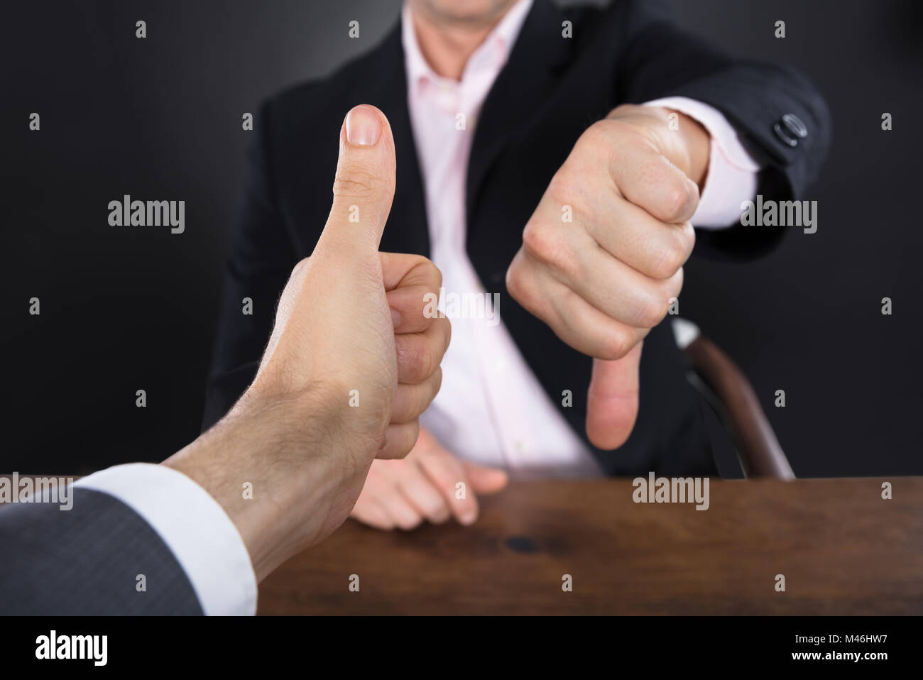 Deux mains d'affaires Showing Thumb Up et le pouce vers le bas sur un bureau en bois Banque D'Images