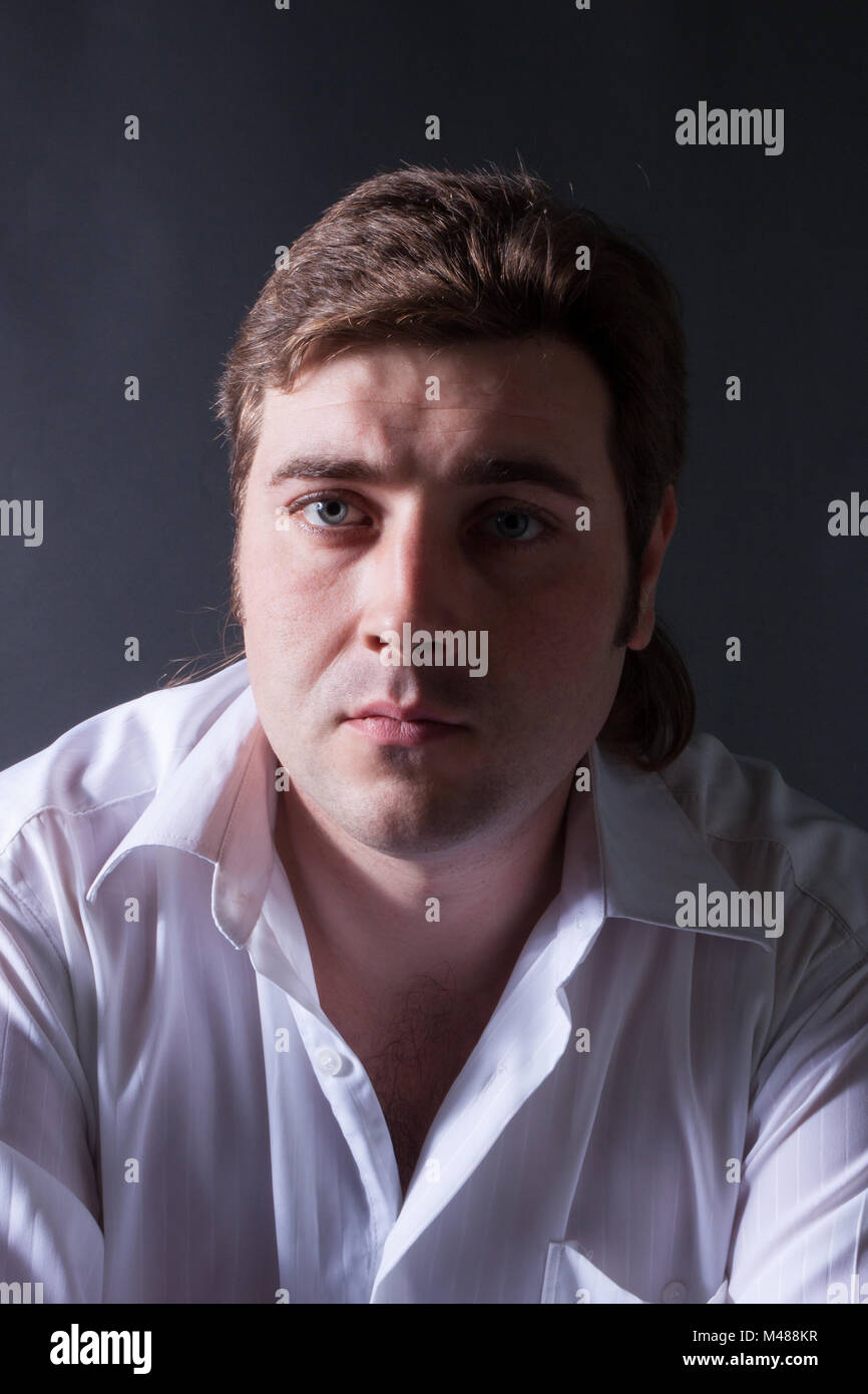 Homme posant en chemise blanche sur fond sombre Banque D'Images